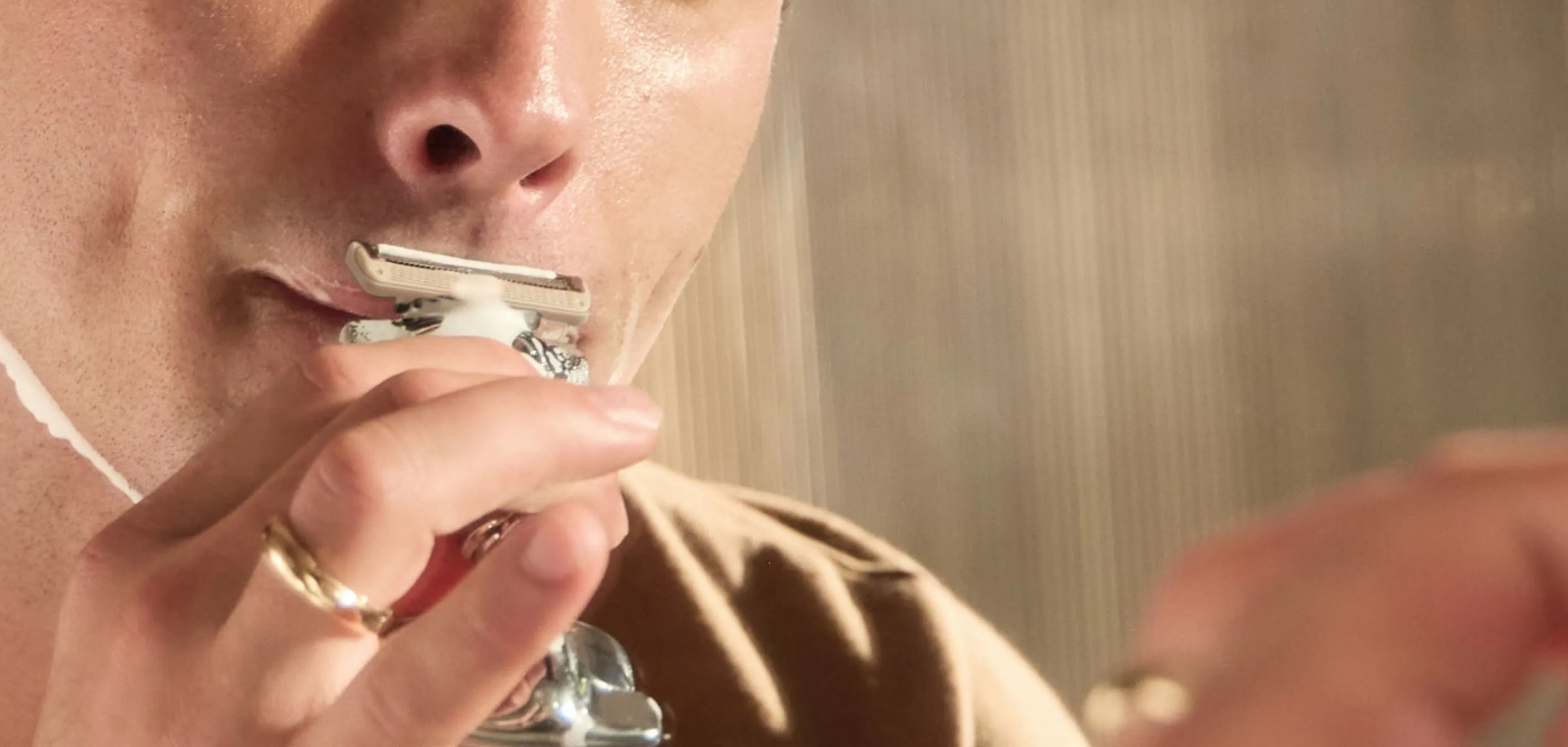 Person shaving with a safety razor in a bathroom setting