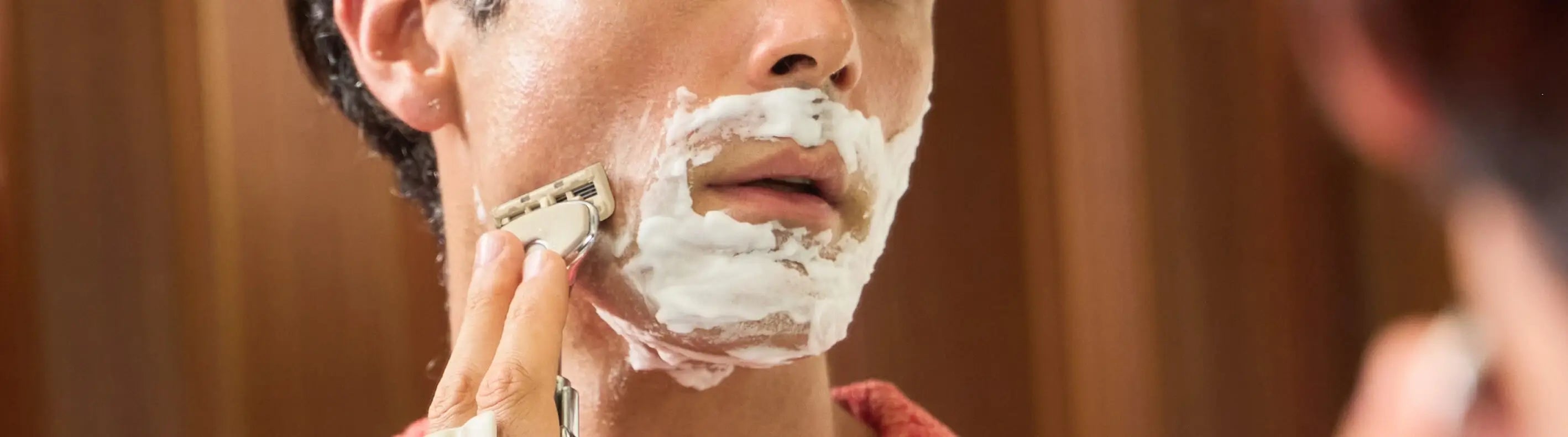 Person applying shaving cream to their face in front of a mirror.