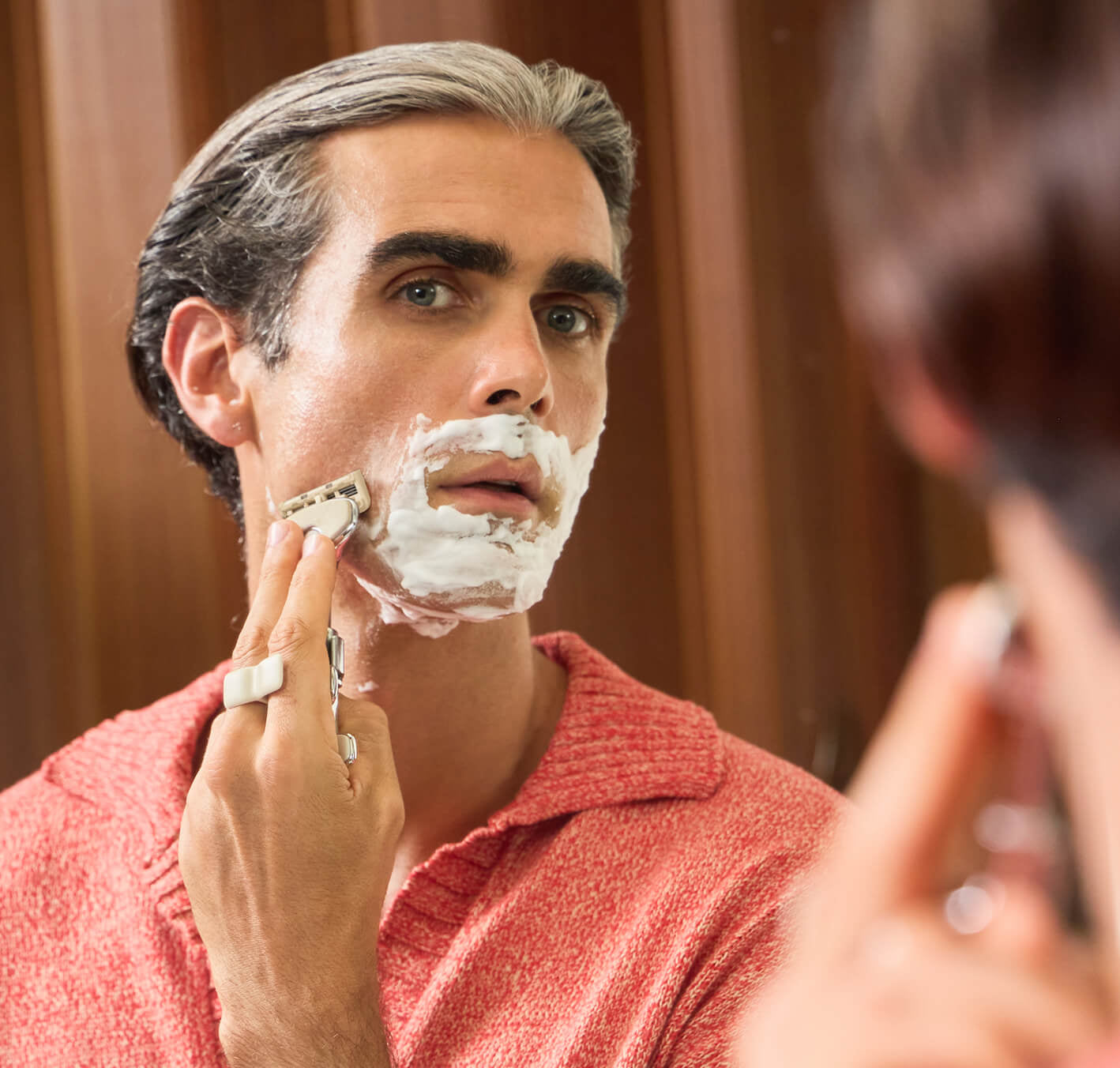 Man shaving his face with a razor in front of a mirror