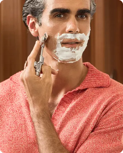 Man shaving his face with a razor, wearing a red robe.