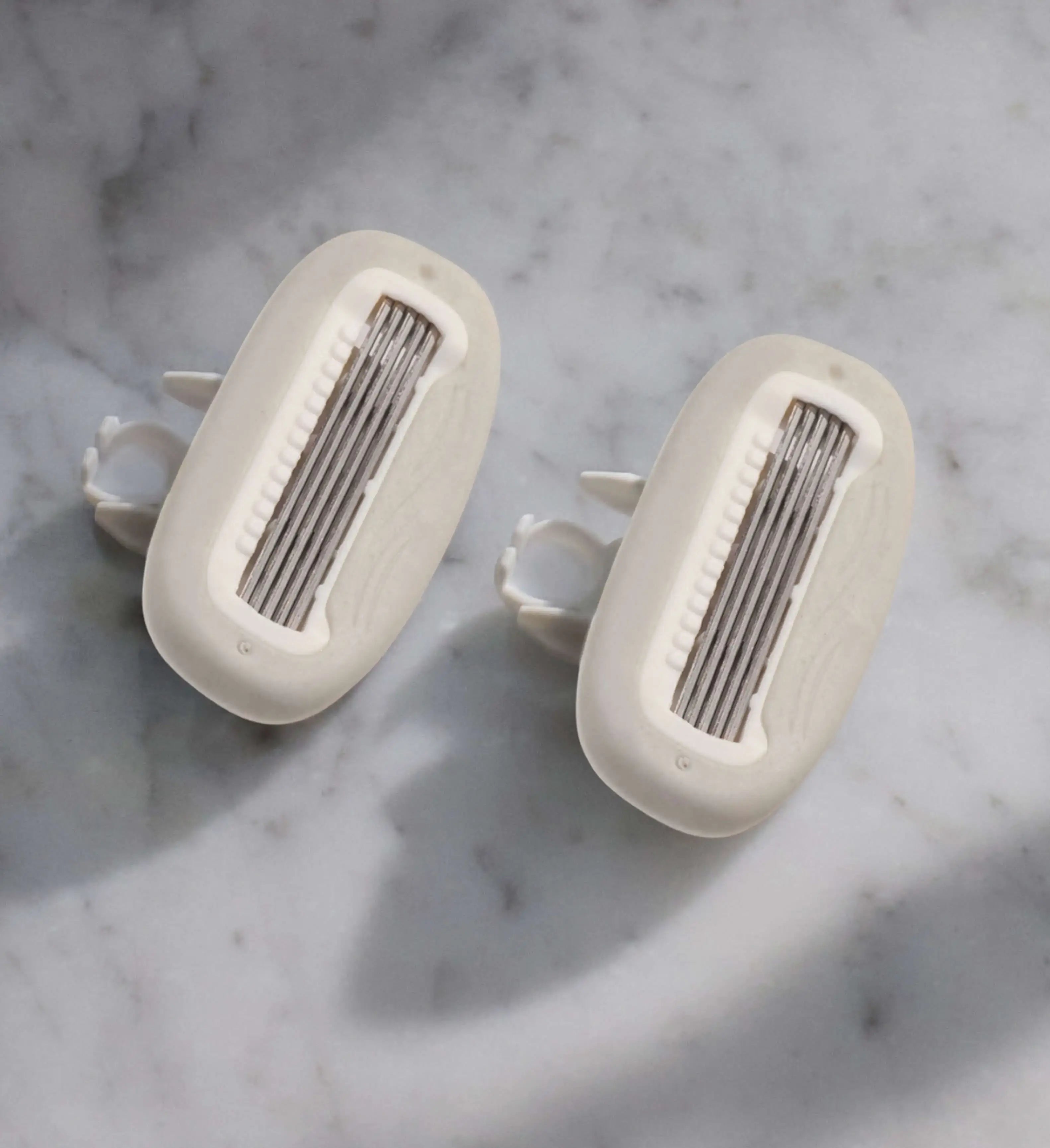 Two razor blade cartridges on a marble countertop