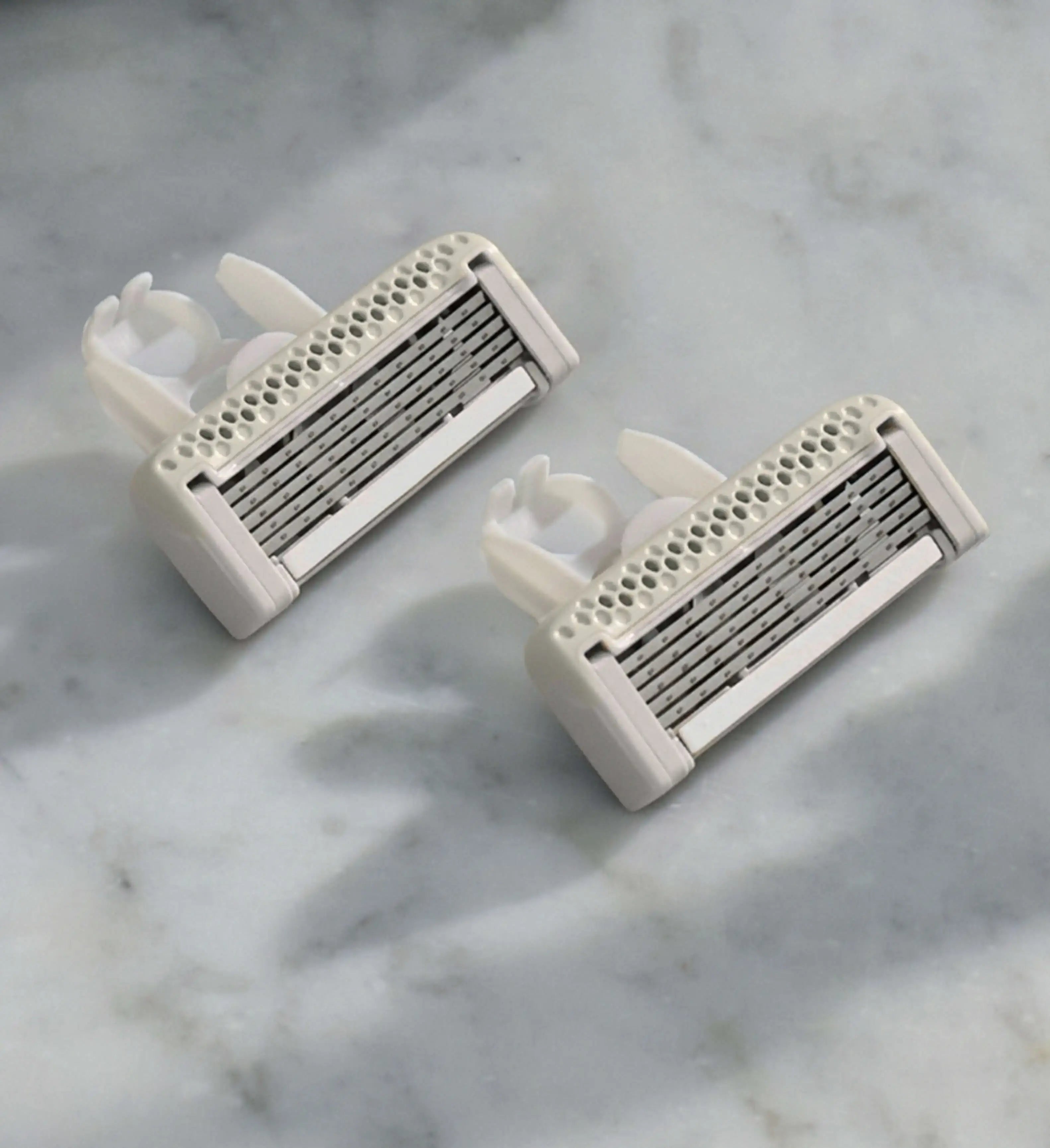 Two white razors with metallic blades on a marble surface