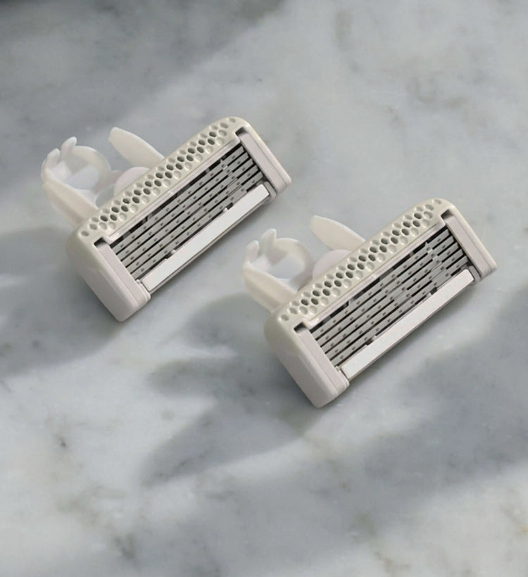 Two white razors with metallic blades on a marble surface